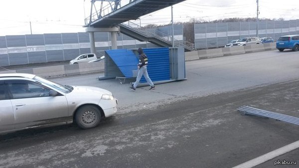 В Новосибирске ветер свалил остановку и бросил на дорогу. Парень, похоже, идёт ждать автобус.